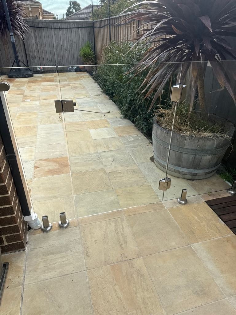 Timber barrel planter standing beside a glass pool gate on a paved side path