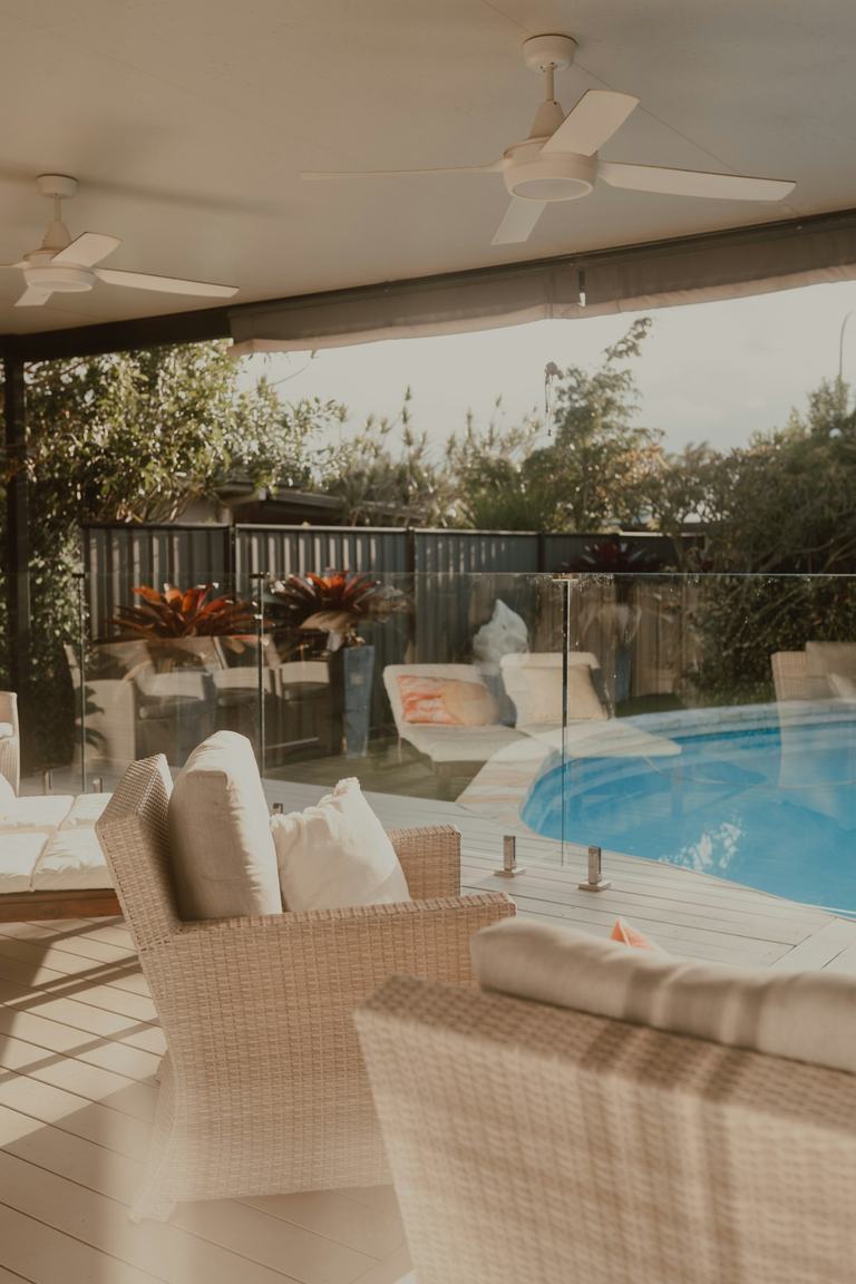 Wicker outdoor chairs close to a glass pool fence on a covered patio