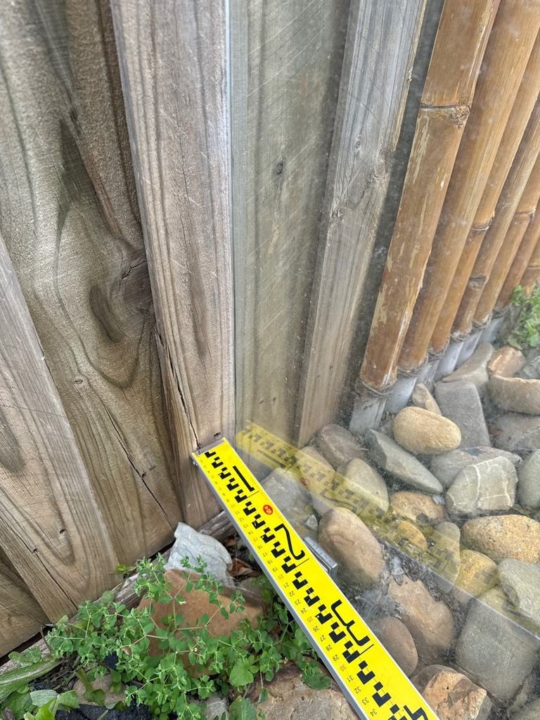 Yellow measuring tape laid along the gap where a timber fence meets a glass pool barrier