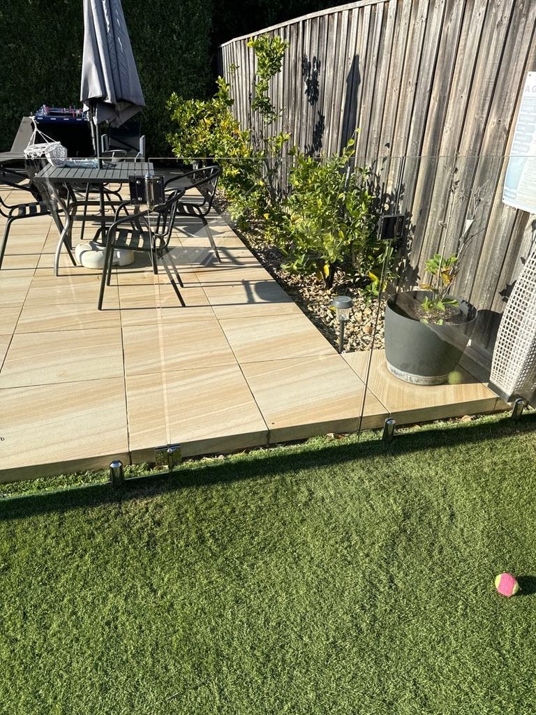 Glass pool gate and fence panels along a paved patio with artificial lawn in front