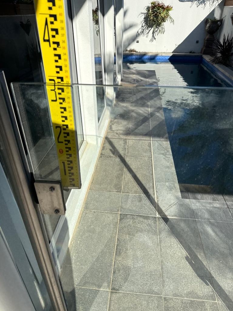 Measuring staff held against a glass pool barrier beside a narrow pool