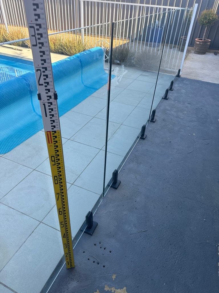 Measuring staff standing against a frameless glass pool fence beside a covered pool