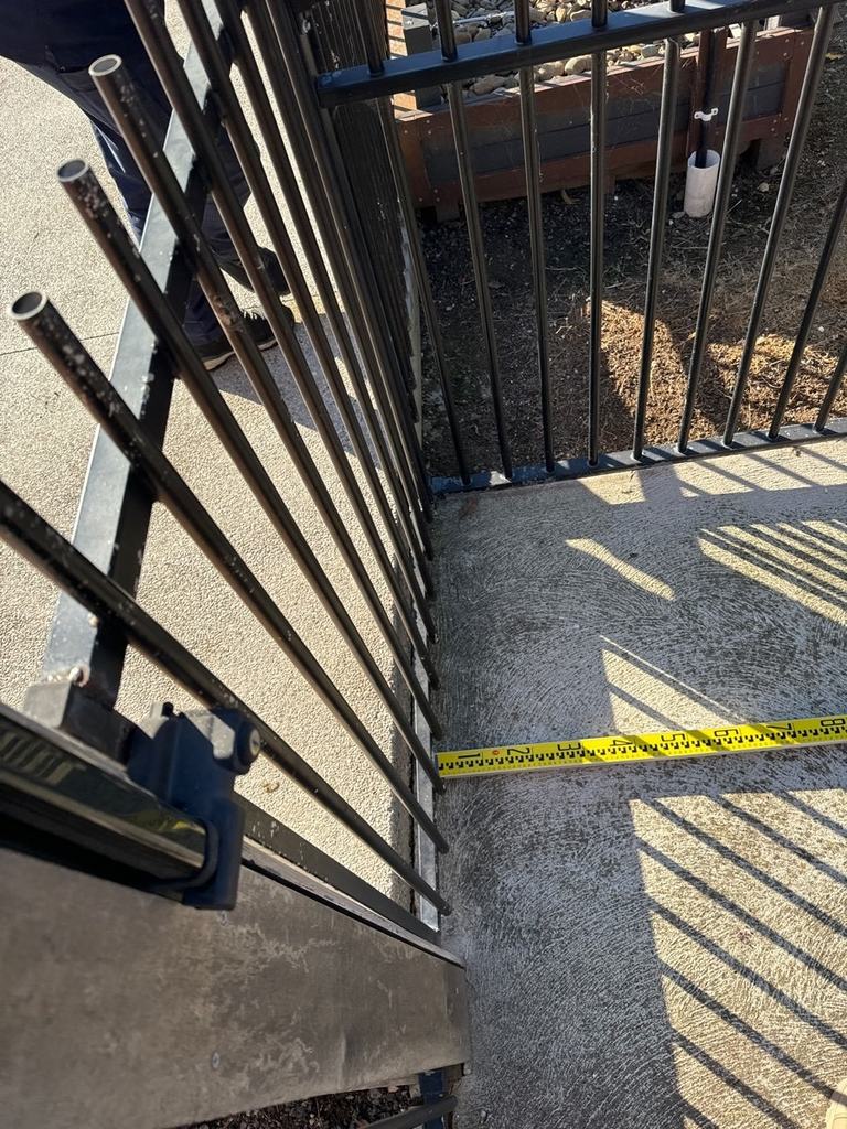 Yellow tape measure on the ground running out from a black tubular pool fence