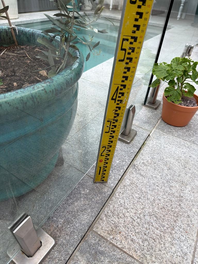 Measuring staff beside a large planter next to a frameless glass pool barrier